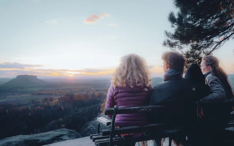 Drei Menschen auf einer Bank am Aussichtspunkt blicken in den Sonnenaufgang