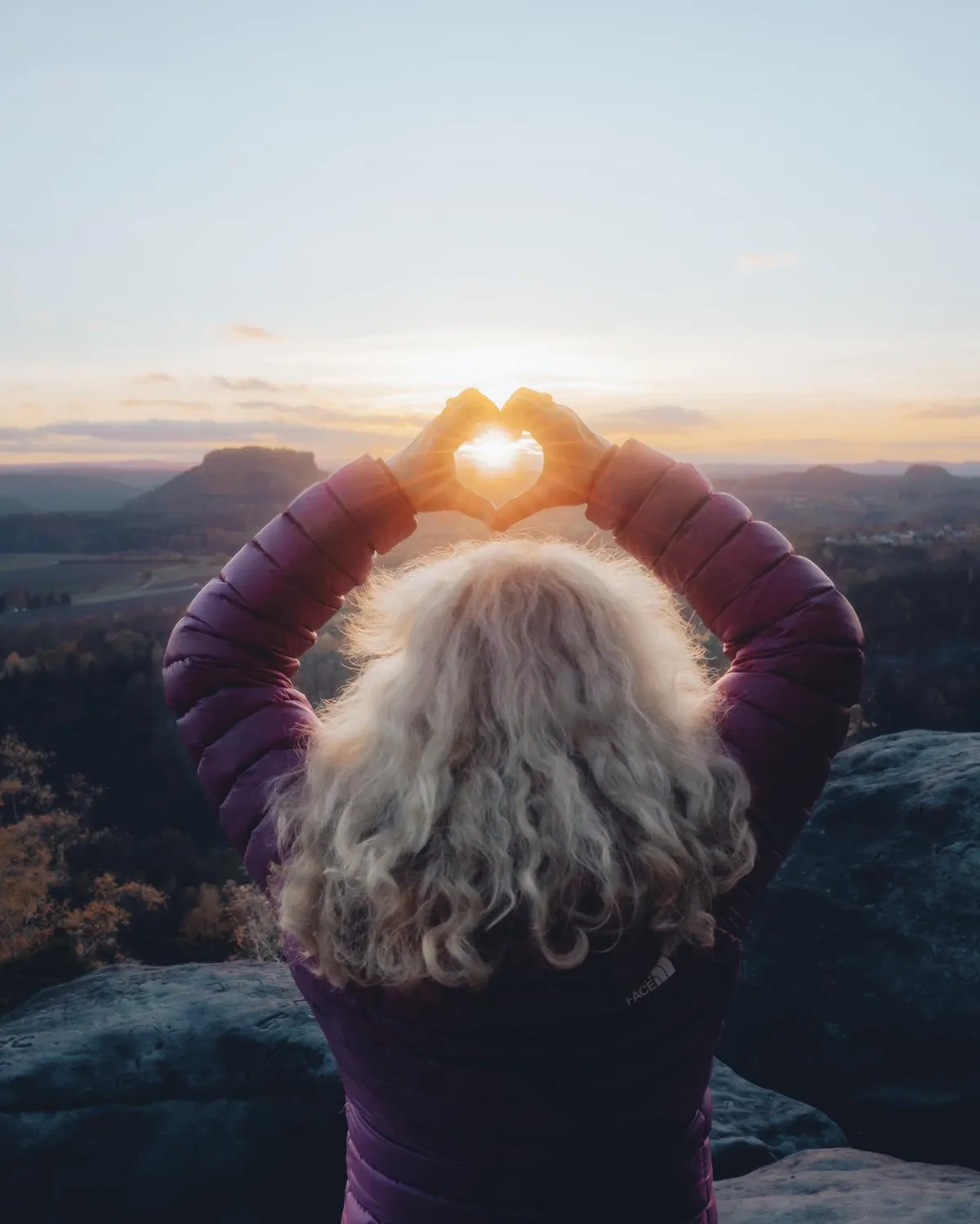 Frau formt bei Sonnenaufgang mit den Händen ein Herz, durch das die Sonne scheint