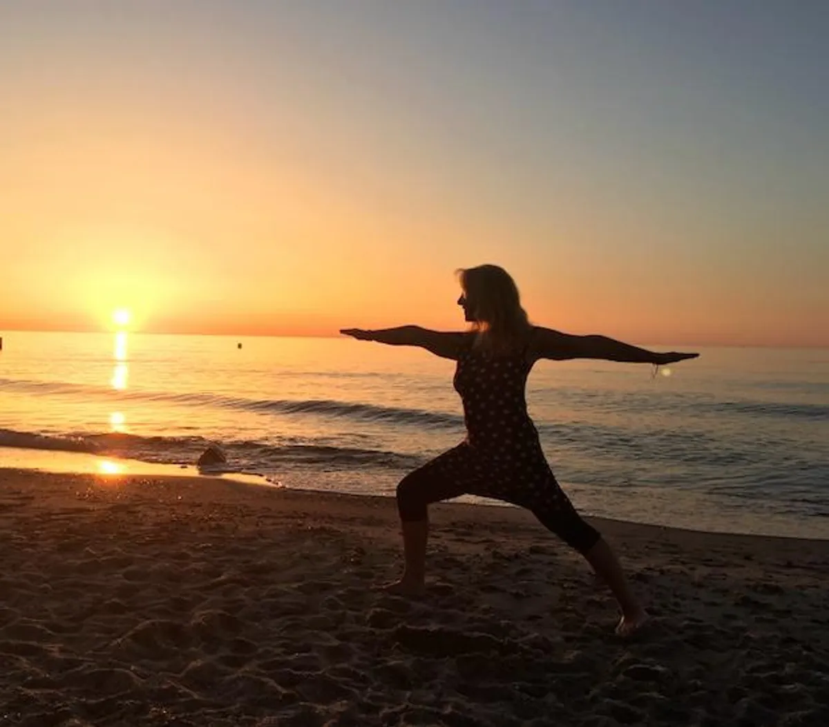 Frau in der Kriegerhaltung am Strand im Gegenlicht des Sonnenuntergangs