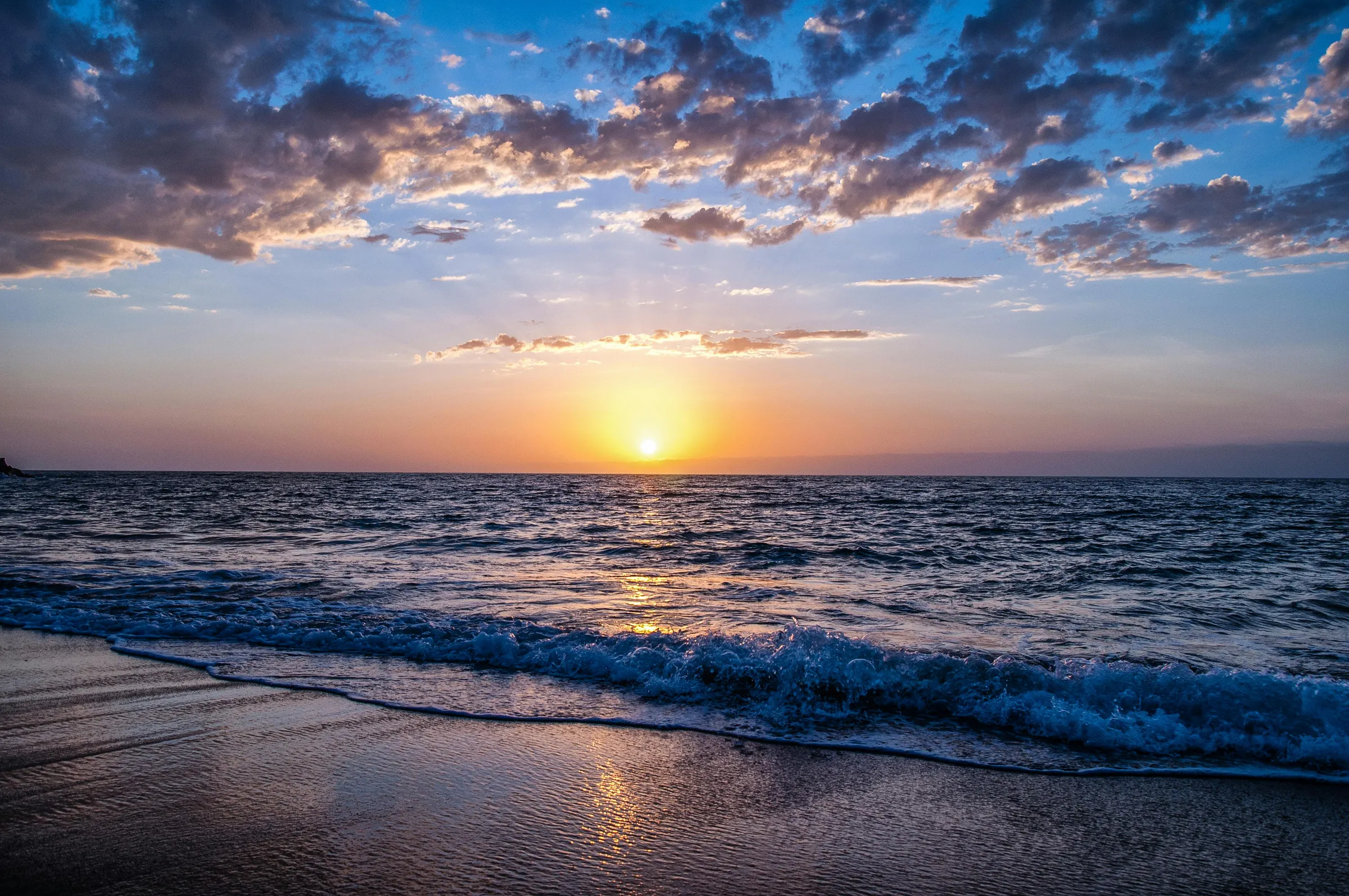 Sonnenuntergang über dem Meer, Wellen laufen sanft am Strand aus